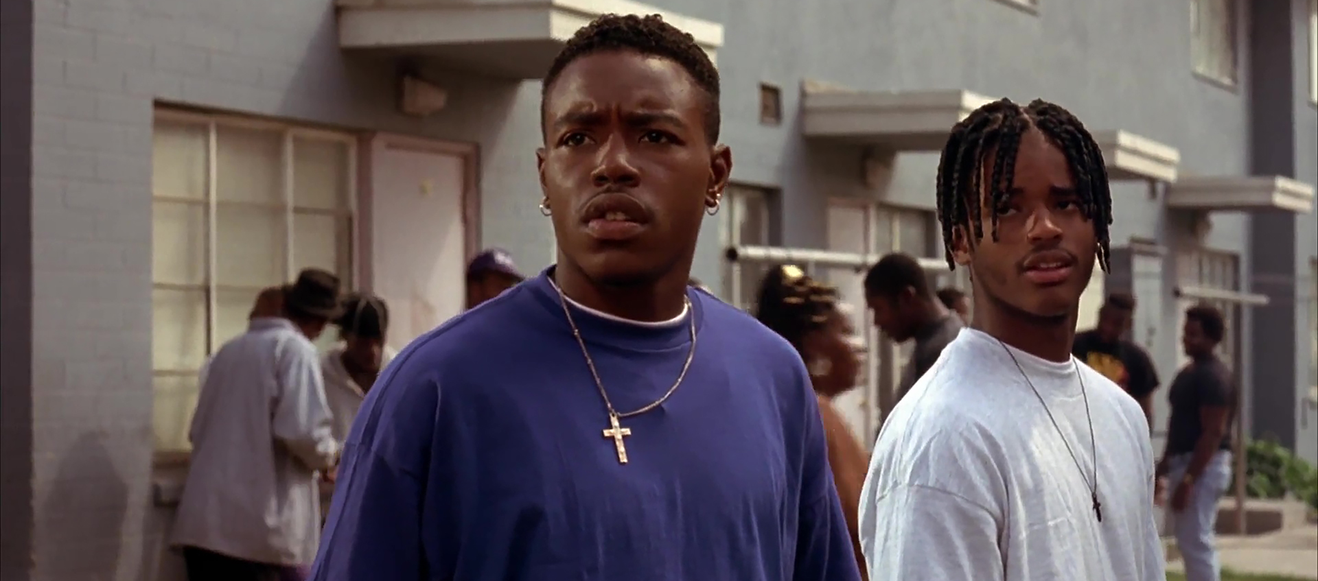 Two young Black men stand together in front of an apartment building