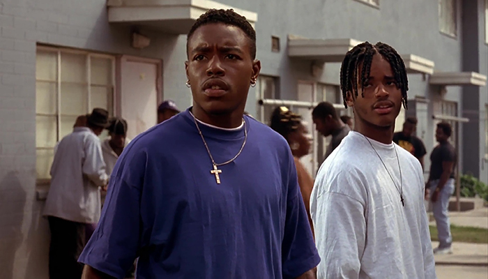 Two young Black men stand together in front of an apartment building