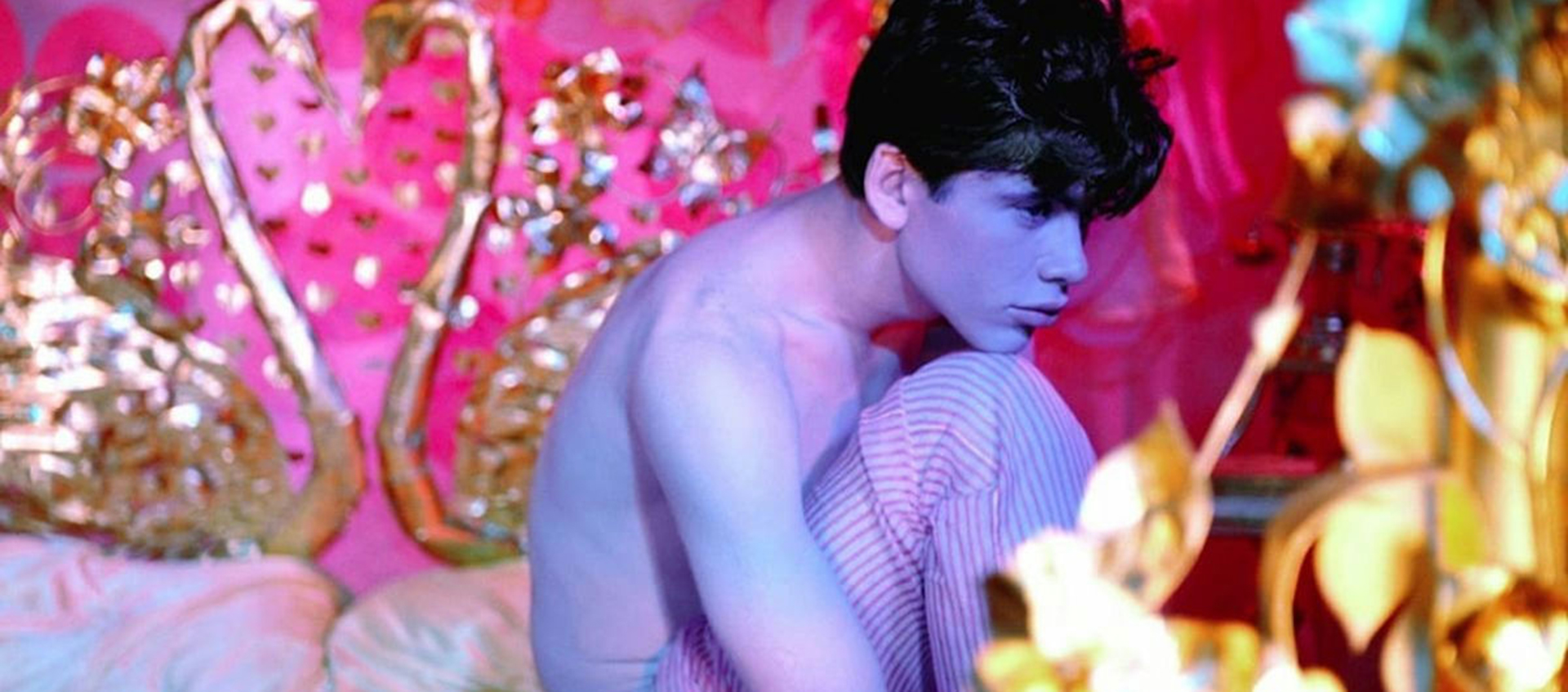 A young man sits on a bed in an ornately decorated room.