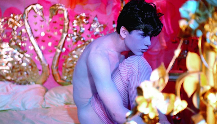 A young man sits on a bed in an ornately decorated room.