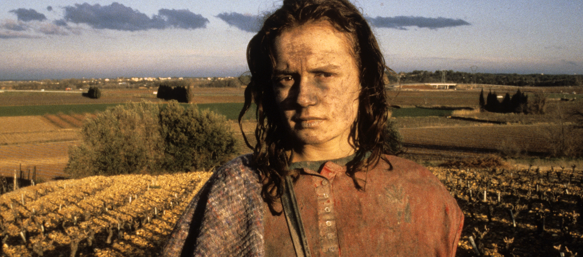 A young woman with dirt on her face and clothes stands in a field.