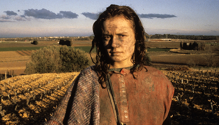 A young woman with dirt on her face and clothes stands in a field.