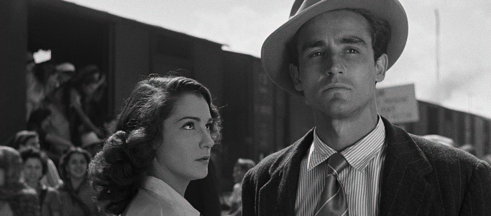 A woman stands looking at a man, behind them many people are leaving a train boxcar.