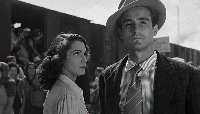 A woman stands looking at a man, behind them many people are leaving a train boxcar.