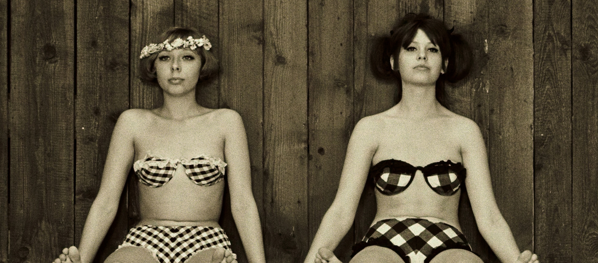 Two women in retro bikinis sit on the ground next to eachother.