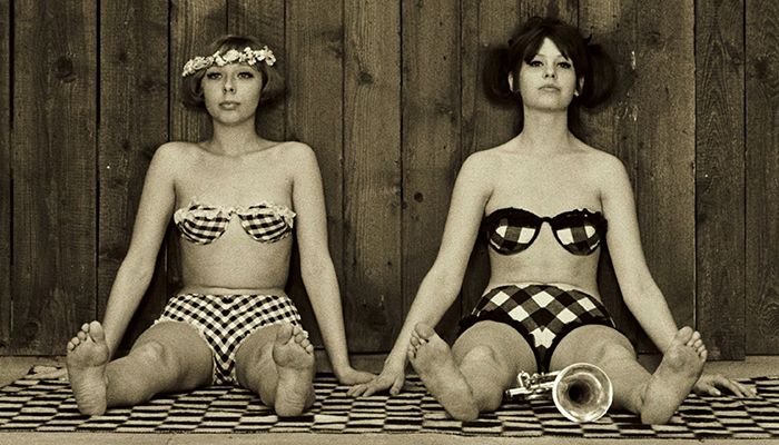 Two women in retro bikinis sit on the ground next to eachother.