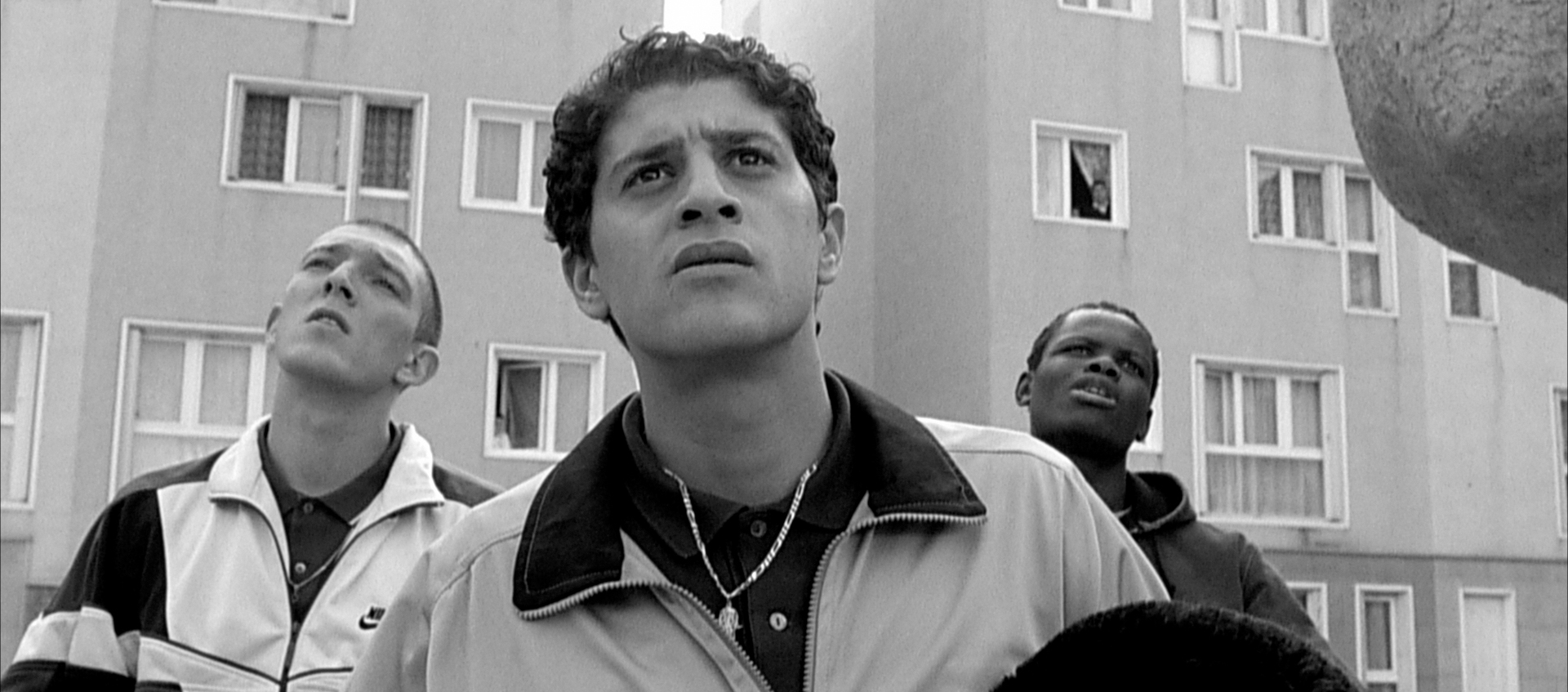 Three men stand in front of a housing project.
