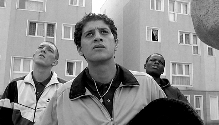 Three men stand in front of a housing project.