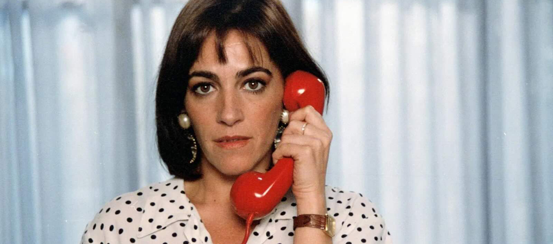 A woman in a polka dot shirt holds a red phone.