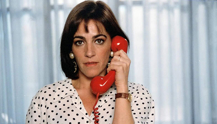 A woman in a polka dot shirt holds a red phone.