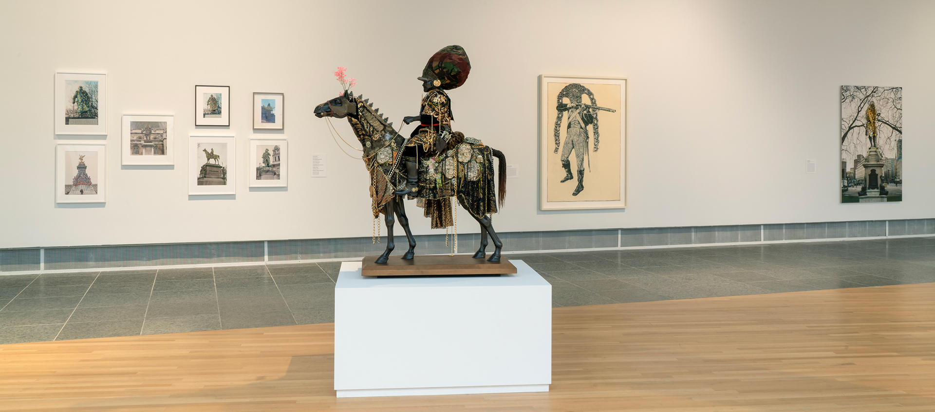 A black equestrian statue of a man in gold-ornamented armor and a large headpiece. The horse is adorned with flowers, gold chains, and medallions.