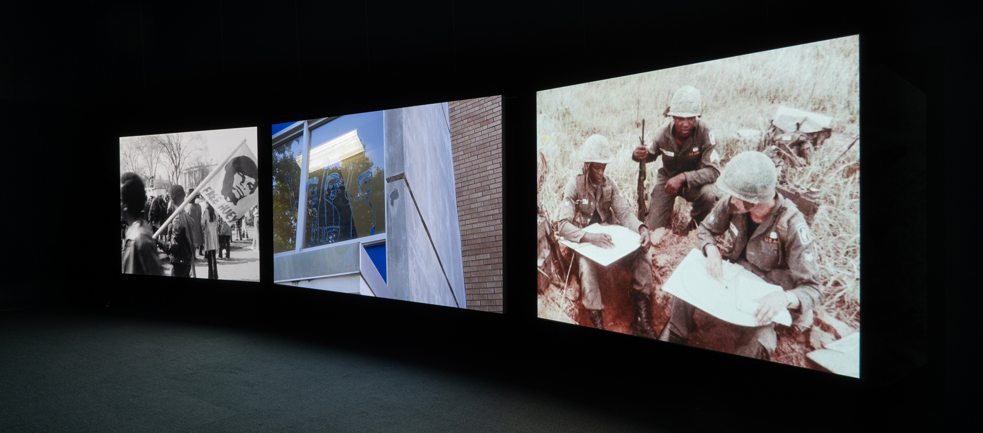 Three large screens project images in a dark room.