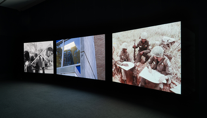 Three large screens project images in a dark room.