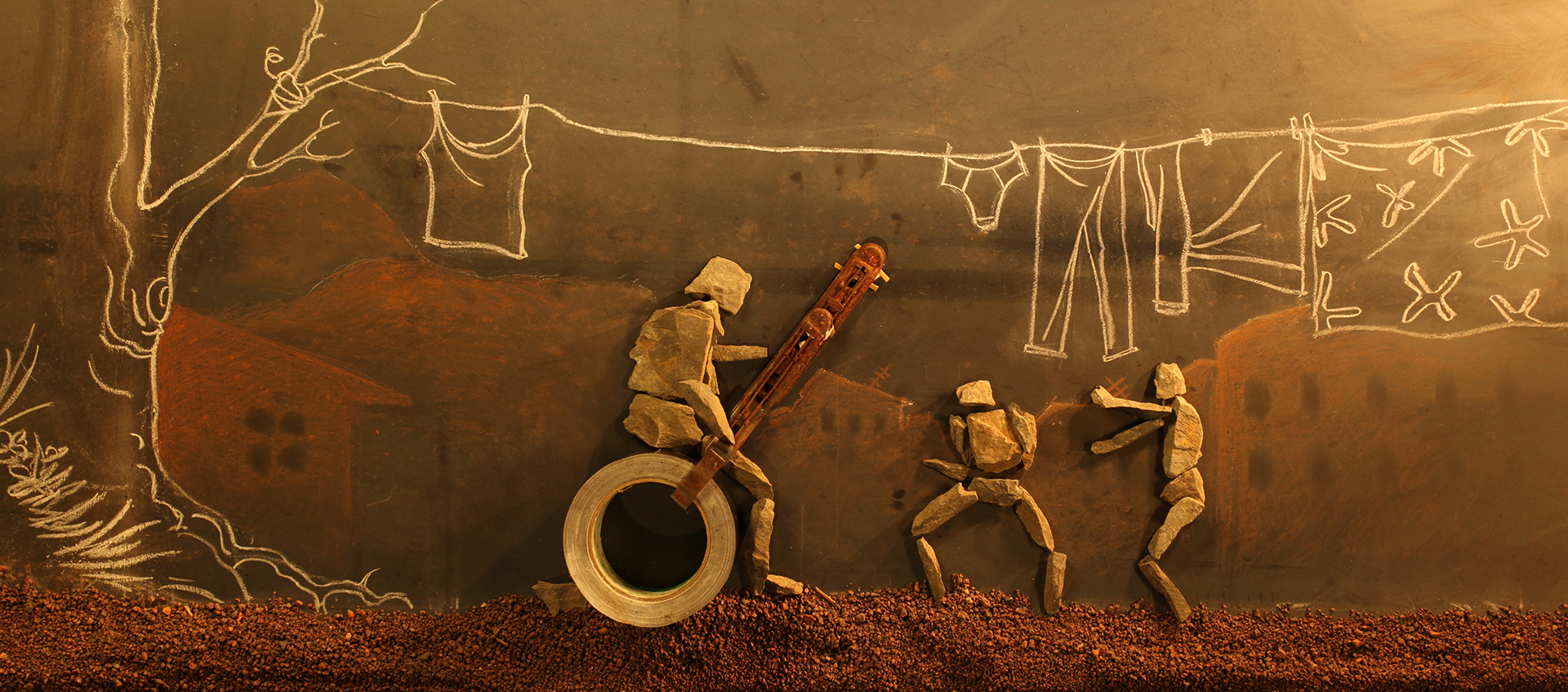 Rock figures are positioned on a blackboard with a chalk drawing of clothes hanging on a line attached to a tree and houses in the background.