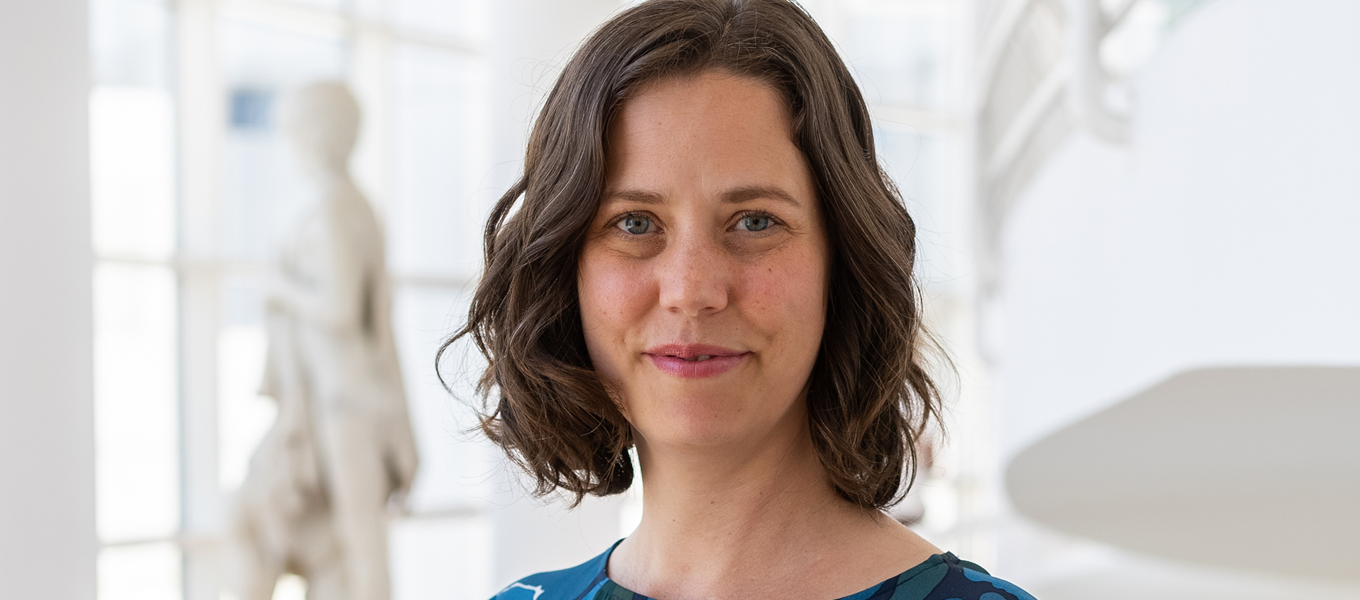 Portrait of Laurel Humble, who has light tan skin, shoulder-length brown hair, grayish-blue eyes, and wears a blue shirt.