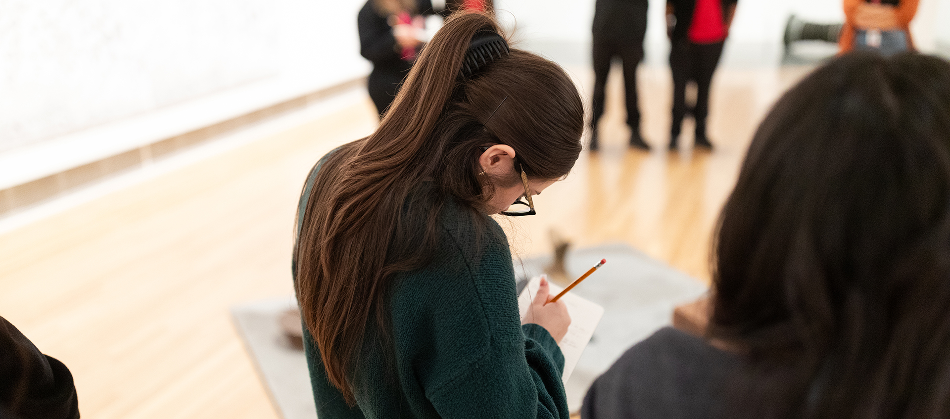 A person stands in a gallery and sketches in a notebook. 