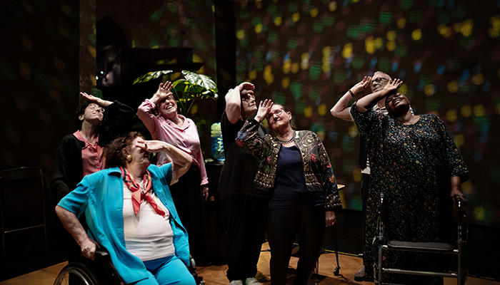 A group of older people stand together with the back of their hands against their foreheads.