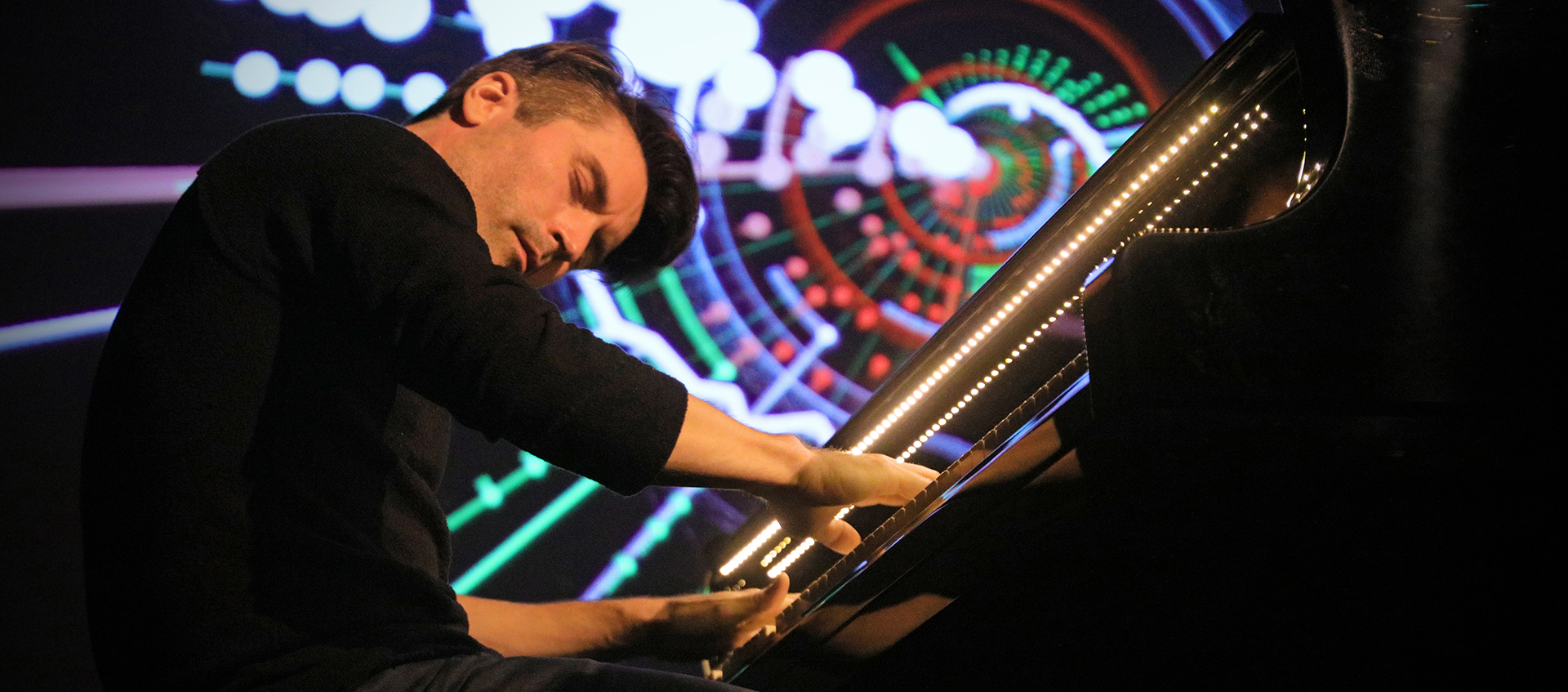A man plays the piano with colorful lights in the background.