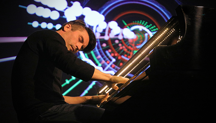 A man plays the piano with colorful lights in the background.