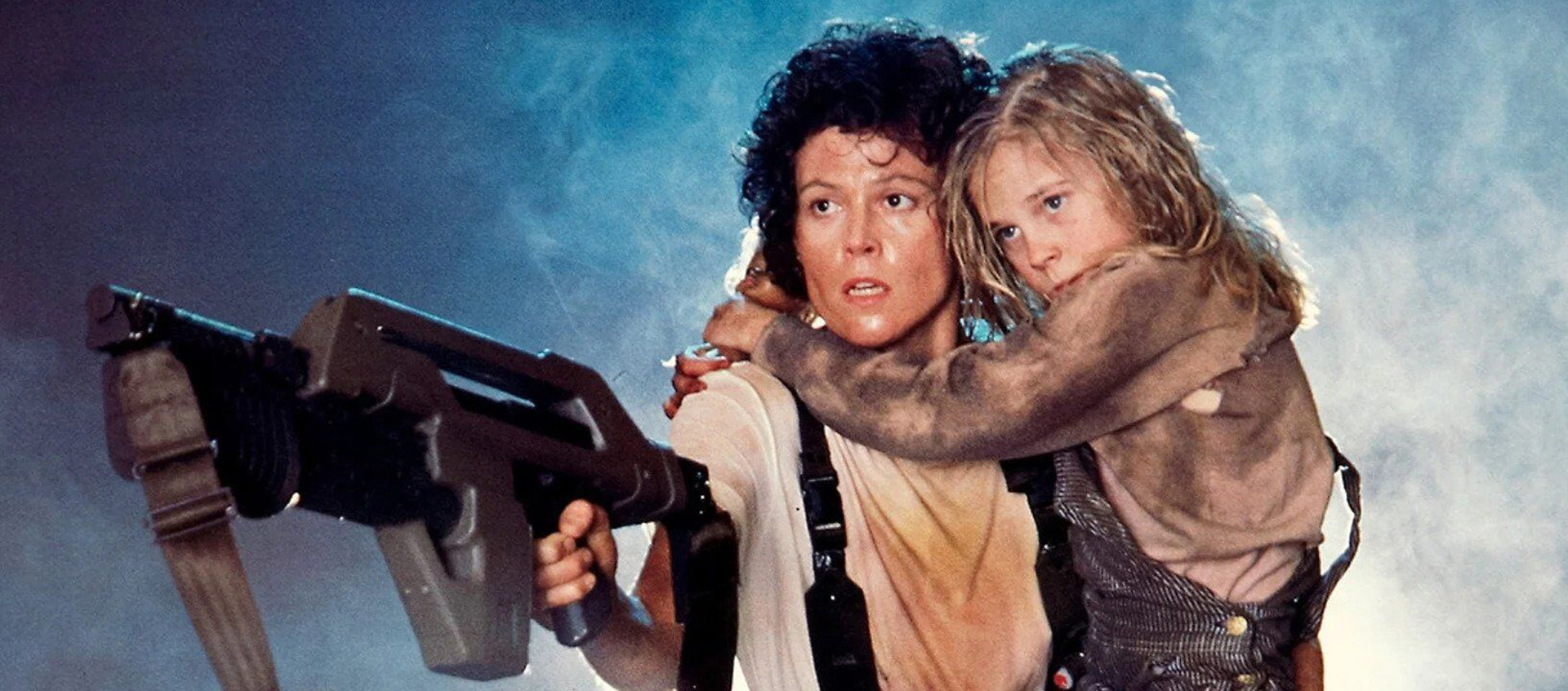 A woman with a dirty white t shirt holds a child and a large gun.