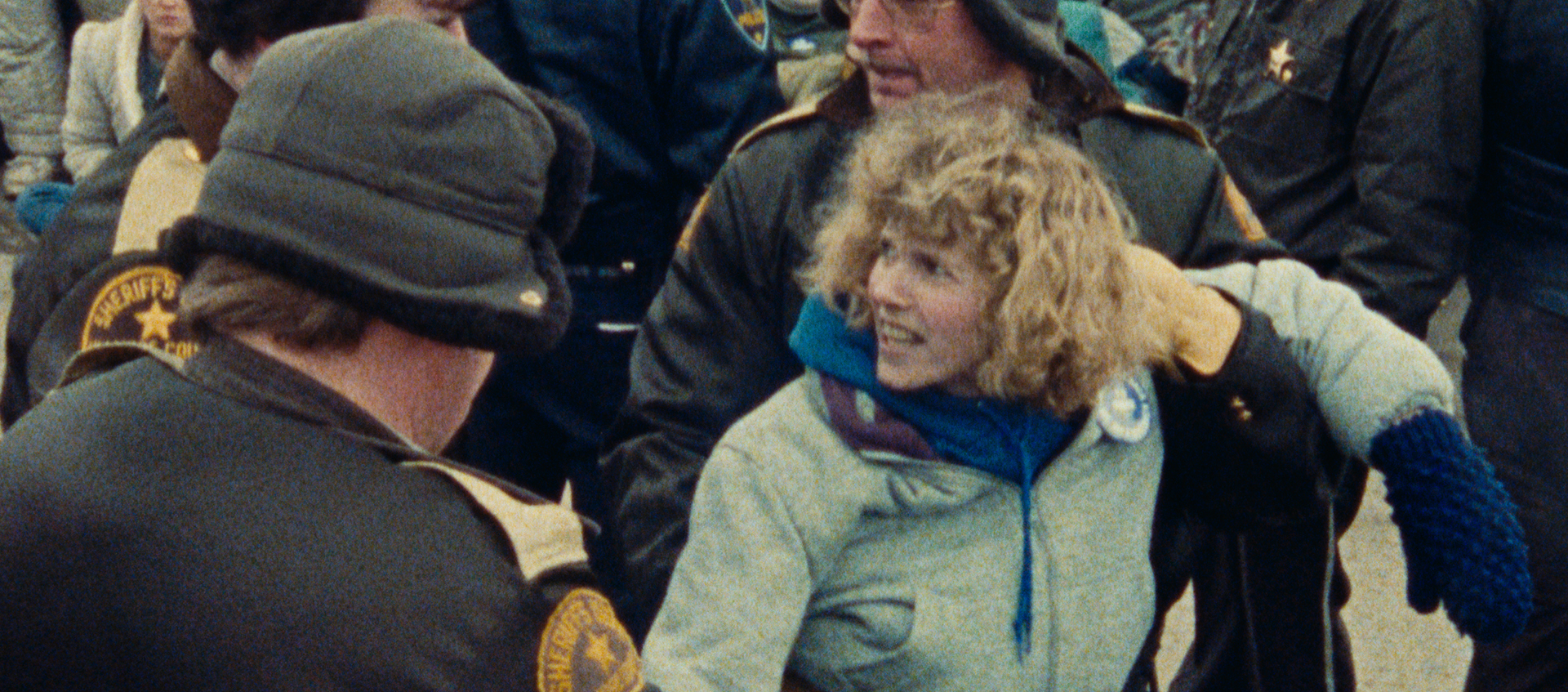 In the midst of a crowd a woman is being restrained by police.