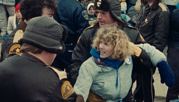 In the midst of a crowd a woman is being restrained by police.
