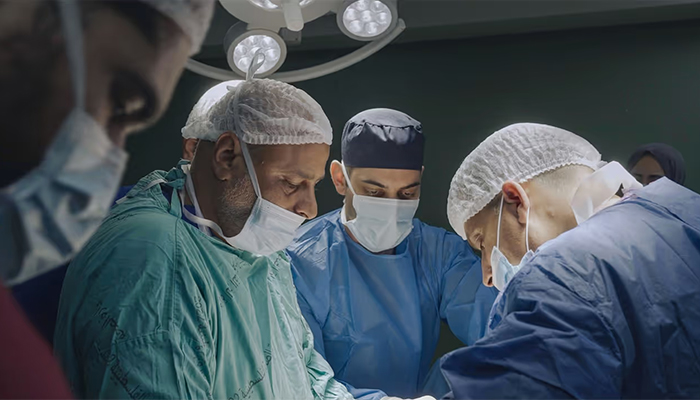 Three doctors wear scrubs and masks in an operating room.