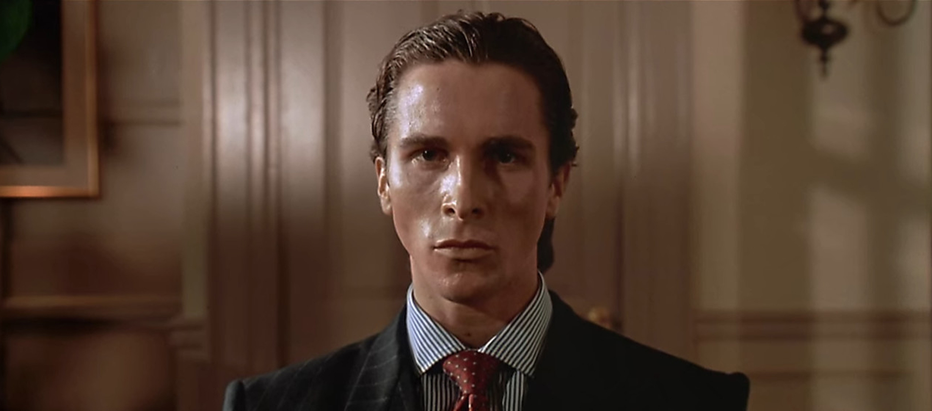 A closeup of Christian Bale with slicked back hair and a suit.