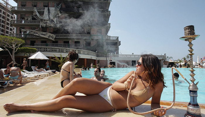 A woman in a bikini lounges by the pool smoking a hookah.