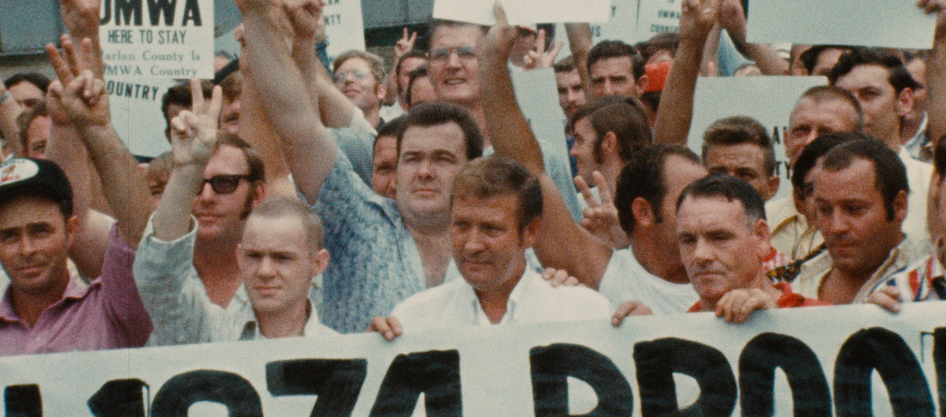 A large group of workers stand together holding signs and holding up peace signs.