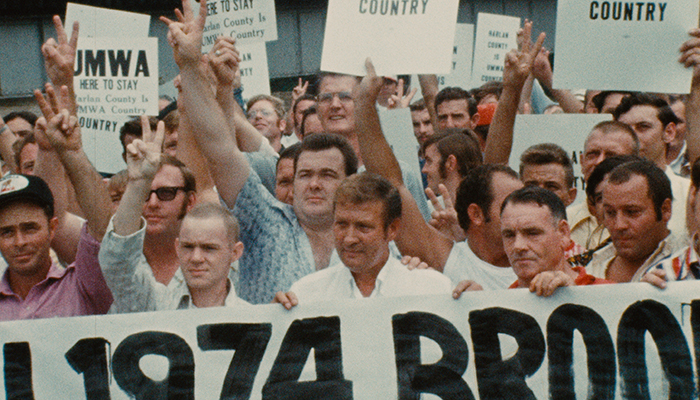A large group of workers stand together holding signs and holding up peace signs.