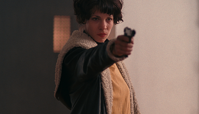 A woman stands with her arm outstretched holding a handgun.