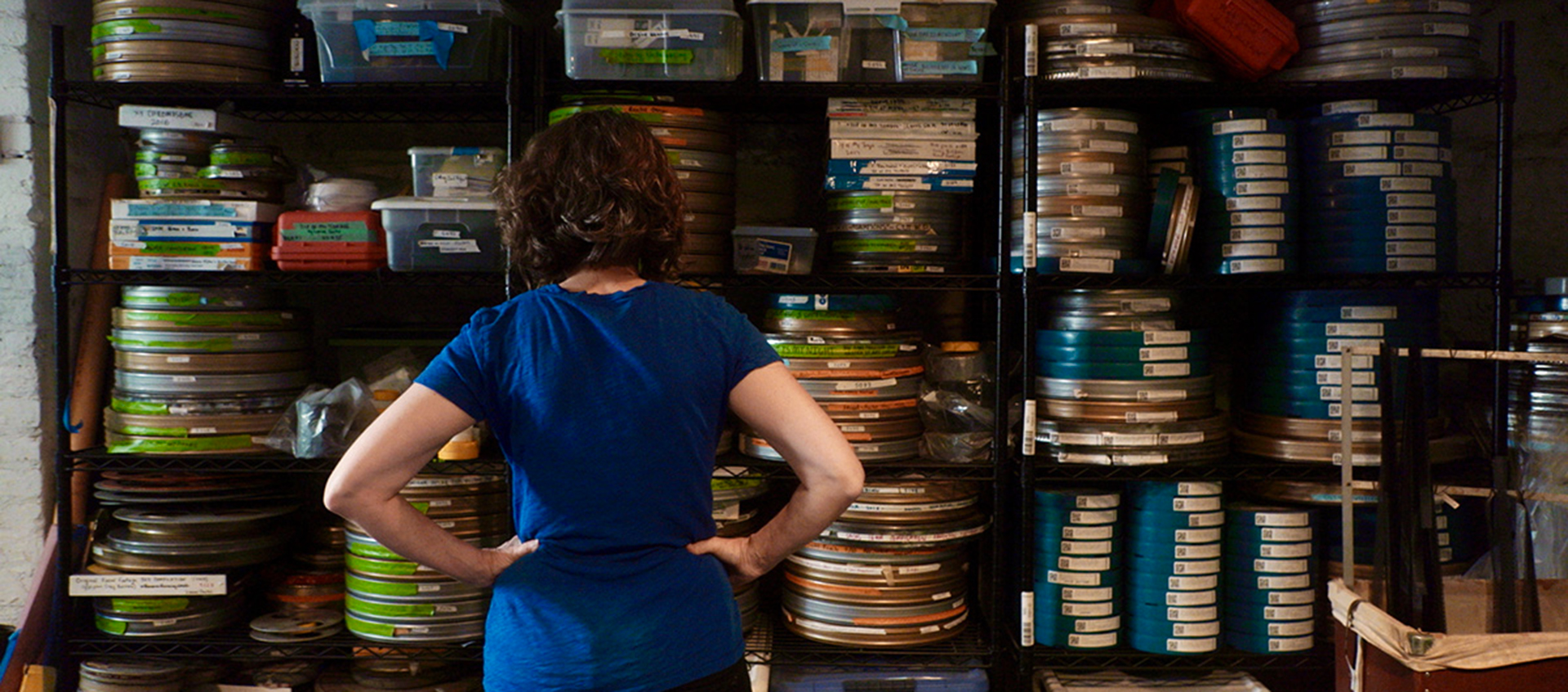 A woman stands facing shelves full of film reel canisters.