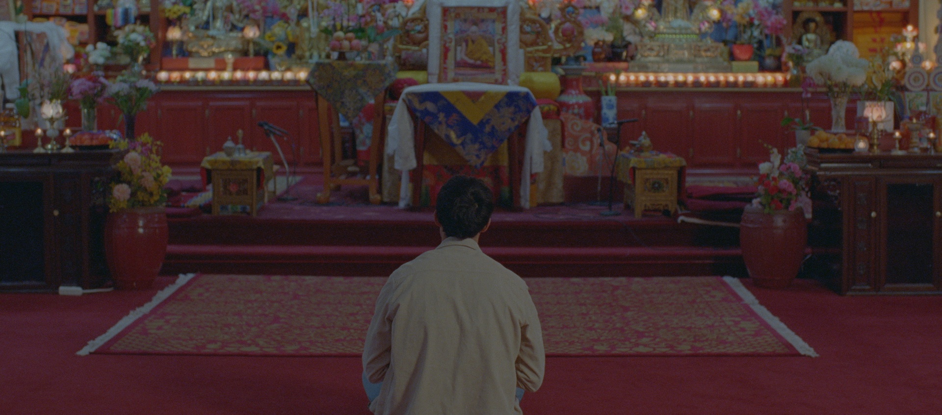 A man sits in front of a colorful buddhist shrine.