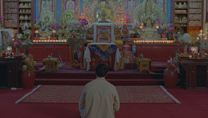 A man sits in front of a colorful buddhist shrine.