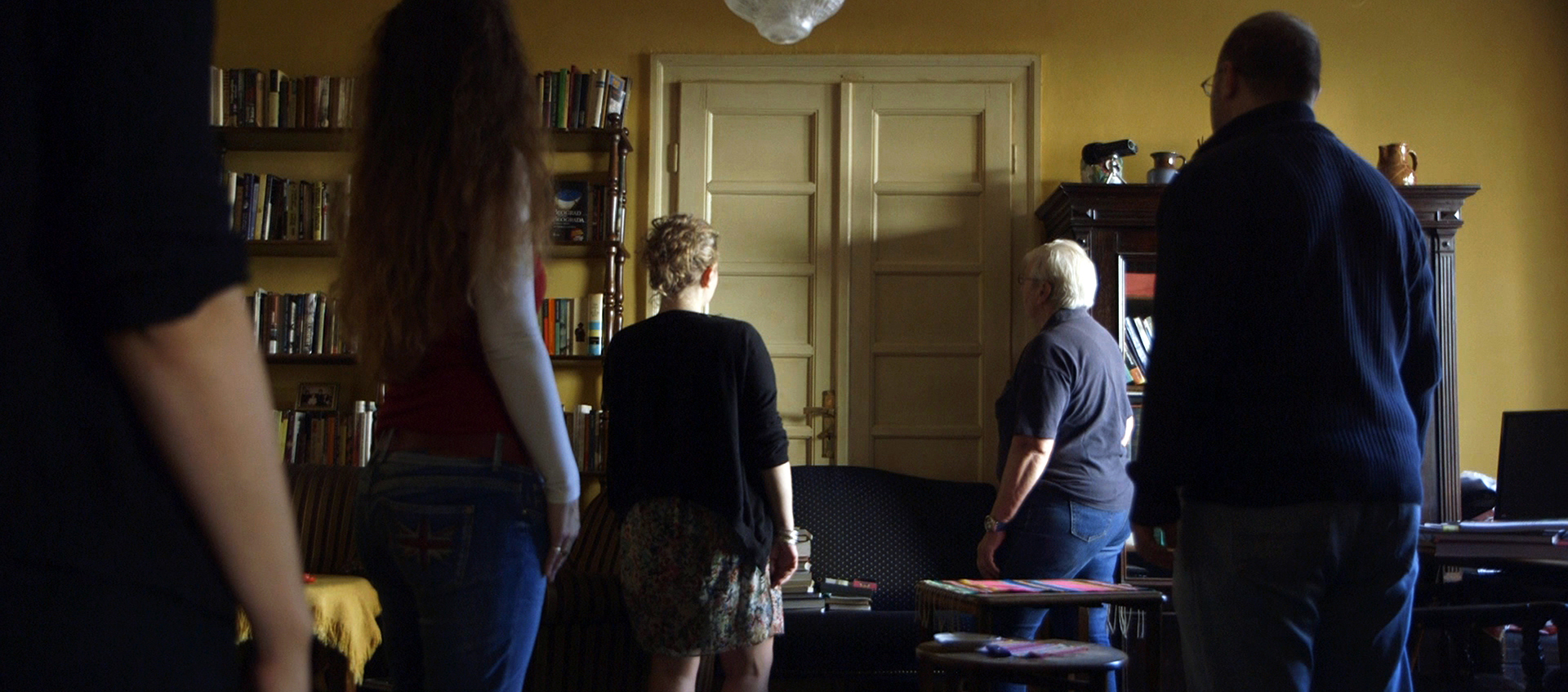 Five people stand in a yellow room facing a closed double door.