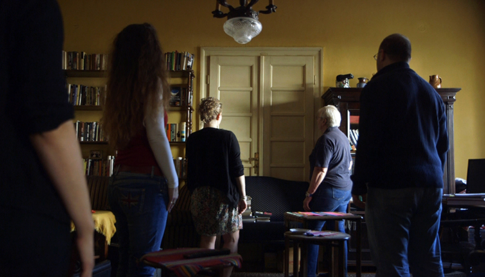 Five people stand in a yellow room facing a closed double door.