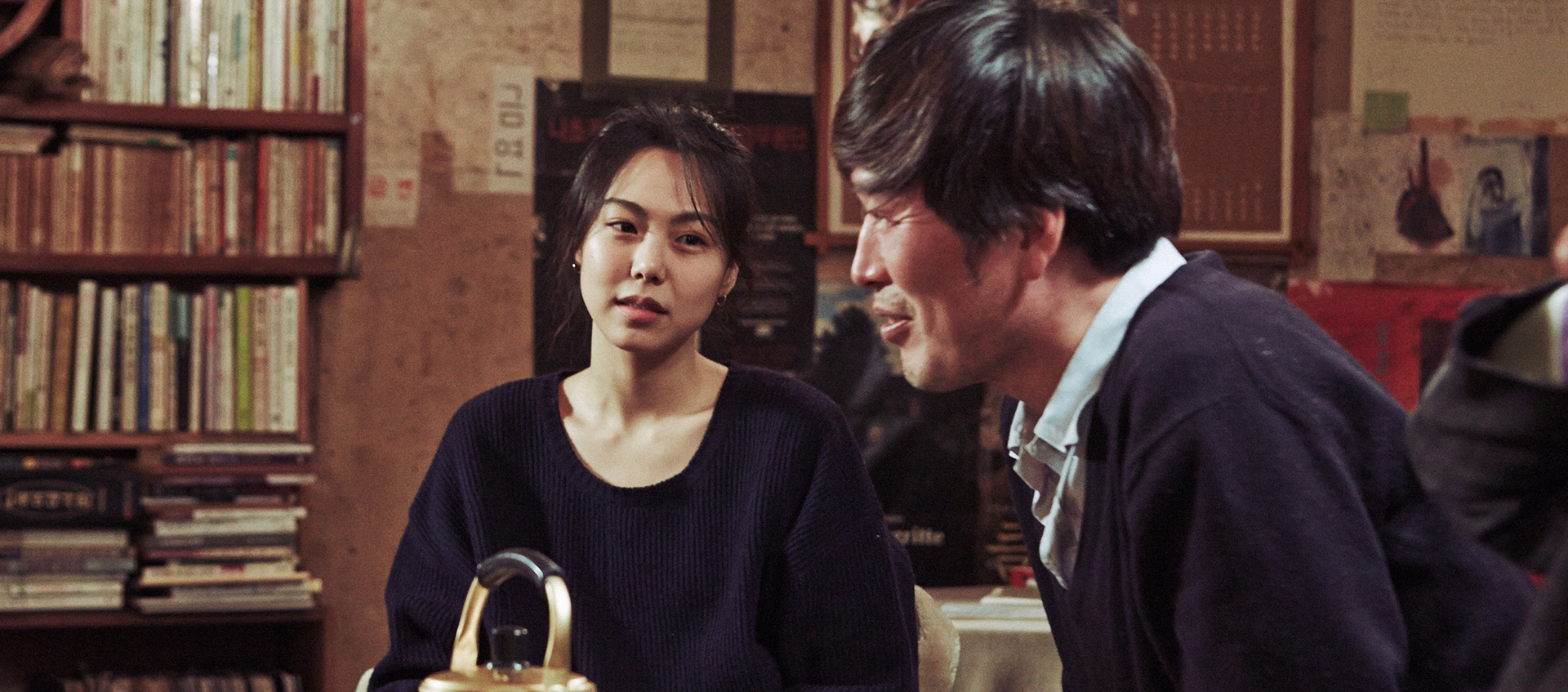 A man and a woman sit together at a table with a tea kettle in front of them.