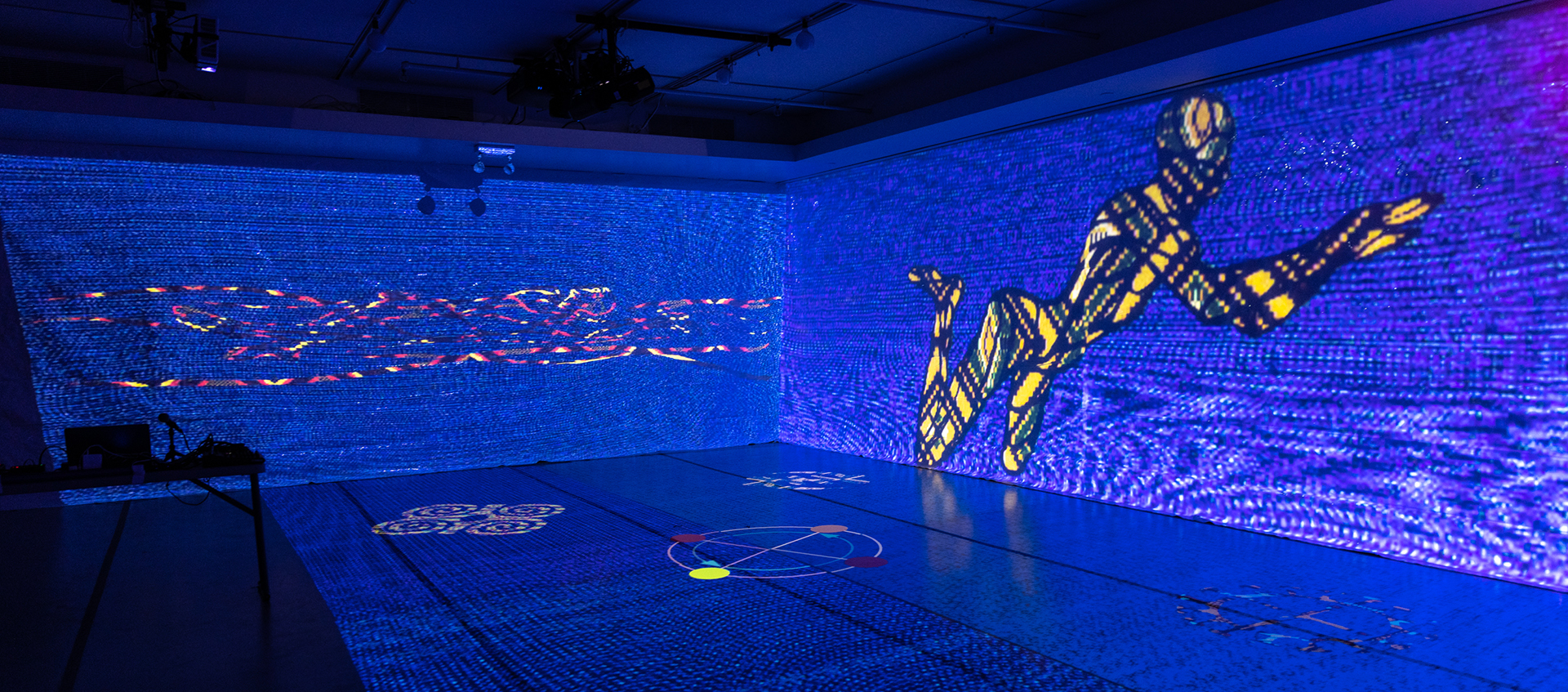 A stage has blue lights and projections of shapes and a person on the floor and the wall.